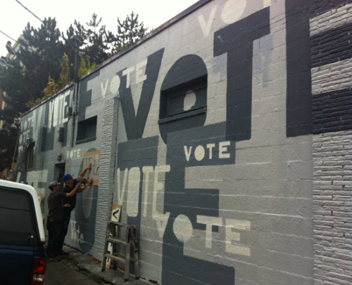 Men spray-painting 'Vote' on the side of a building